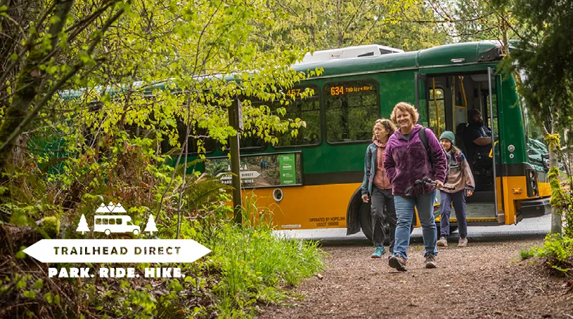 A woman in hiking gear leaves a Trailhead Direct bus at a King County trailhead.