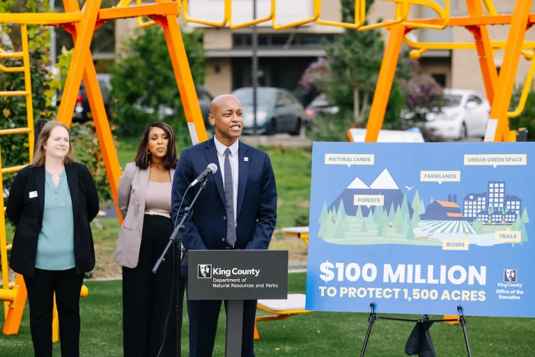 Executive Zahilay speaks at Cheryl Chow Park Next to a sign that says $100 million to protect 1,500 acres.